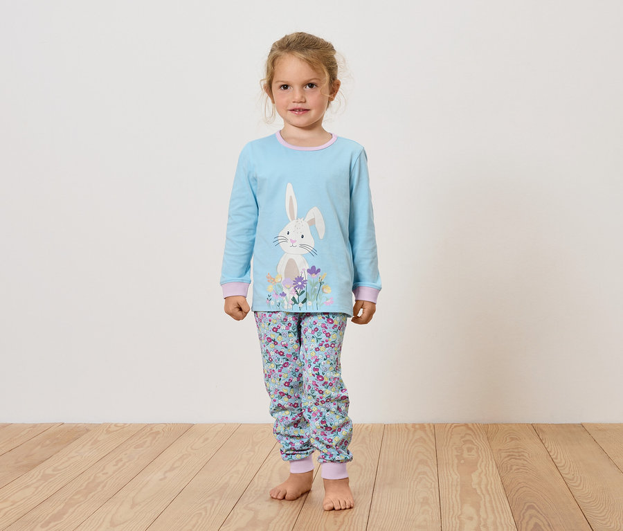 Fille en pyjama bleu clair avec un imprimé de lapin et de fleurs, debout sur un plancher en bois.