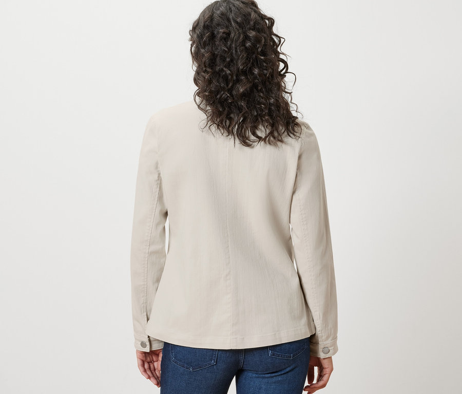 Vue arrière d'une femme aux cheveux bruns ondulés portant une veste en jean avec des poches cargo et un jean bleu.
