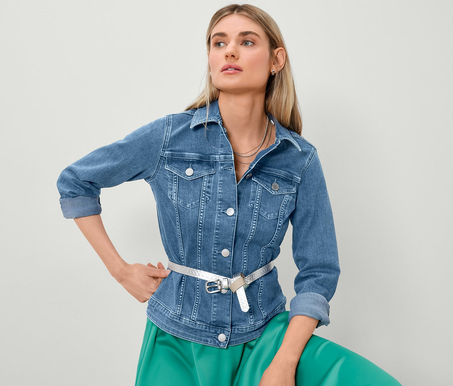 Femme blonde posant en veste en jean et jupe en satin.