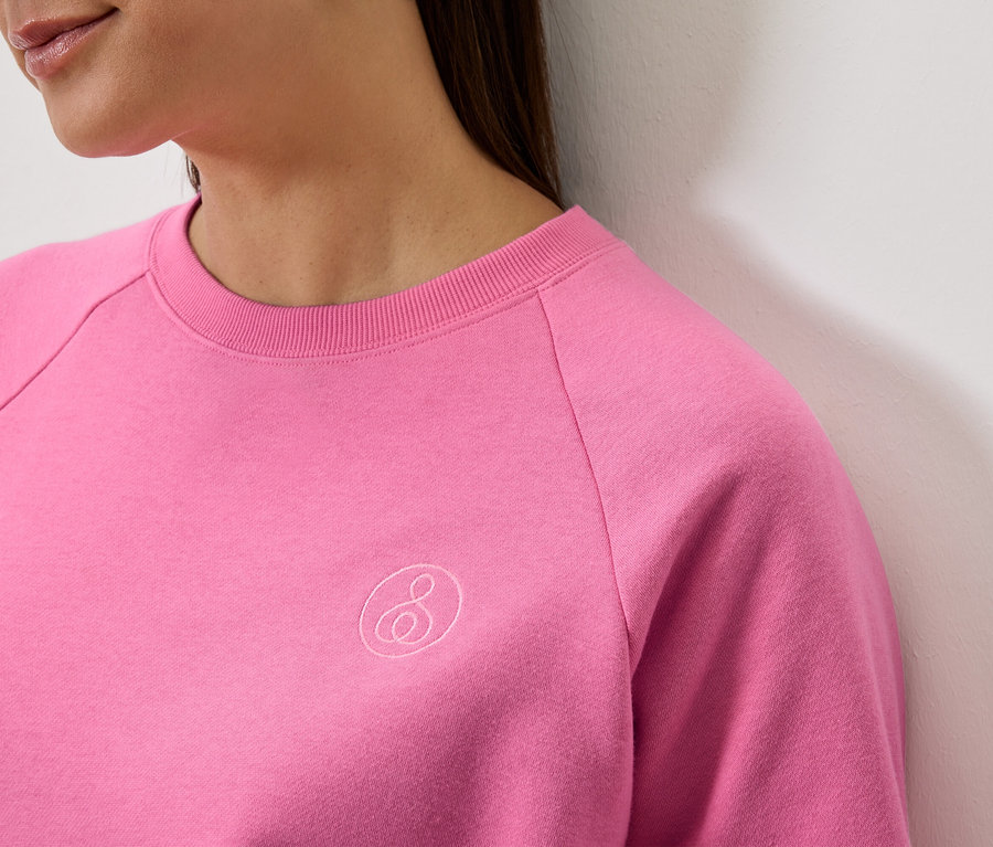 Gros plan d'une femme portant un sweat-shirt rose à manches longues avec un logo.