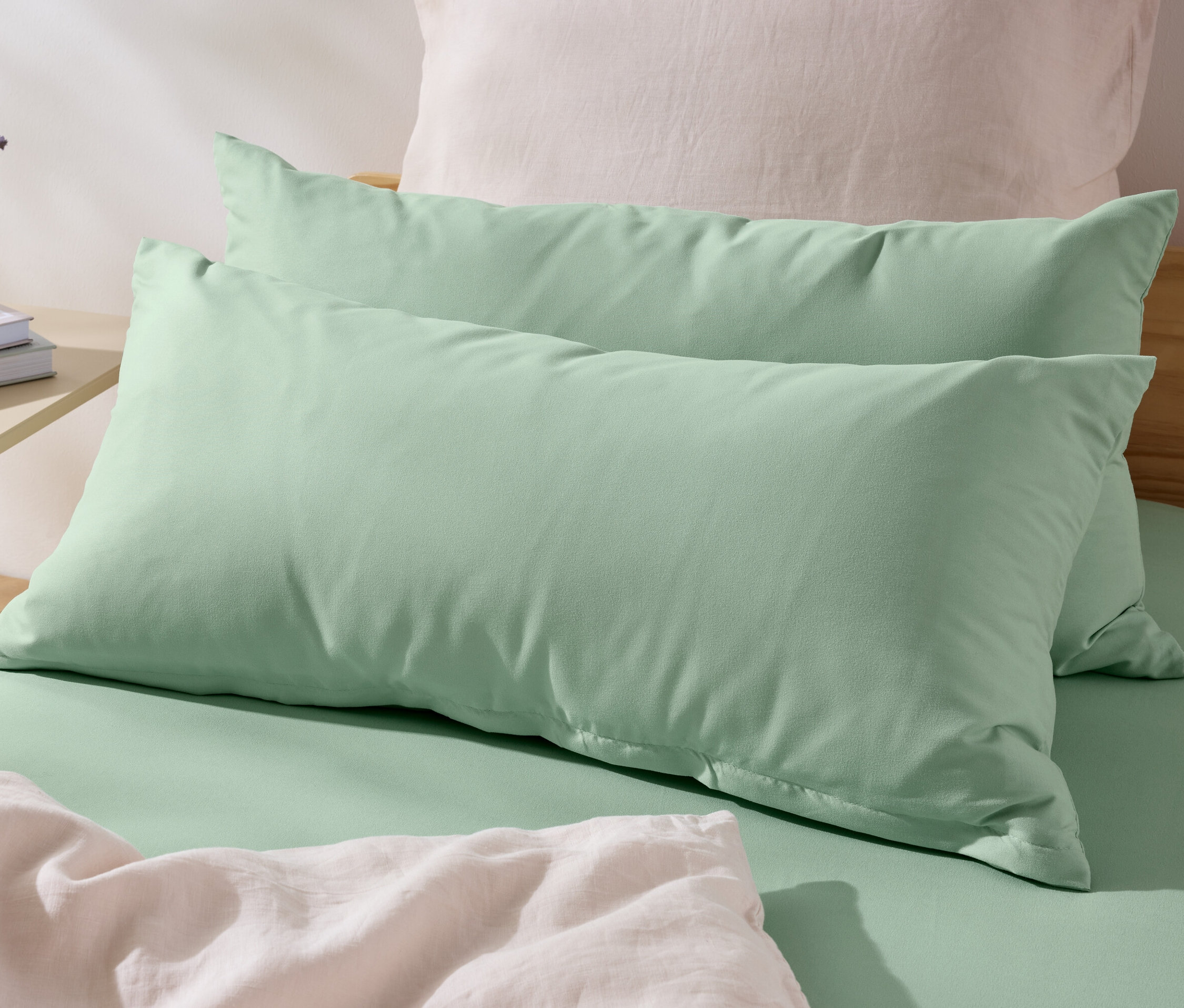 Deux taies d’oreiller vertes en microfibre (env. 80 x 40 cm) sont posées sur un lit. Une vase avec des fleurs et des livres sont sur la table de chevet.