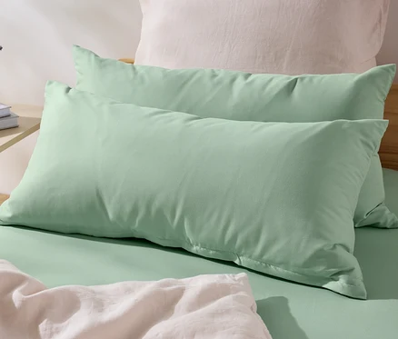 Deux taies d’oreiller vertes en microfibre (env. 80 x 40 cm) sont posées sur un lit. Une vase avec des fleurs et des livres sont sur la table de chevet.