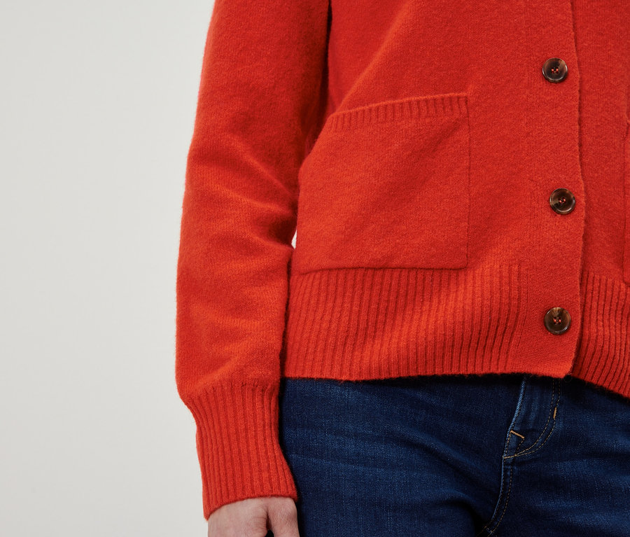 Cardigan rouge avec des boutons marron et un jean bleu.