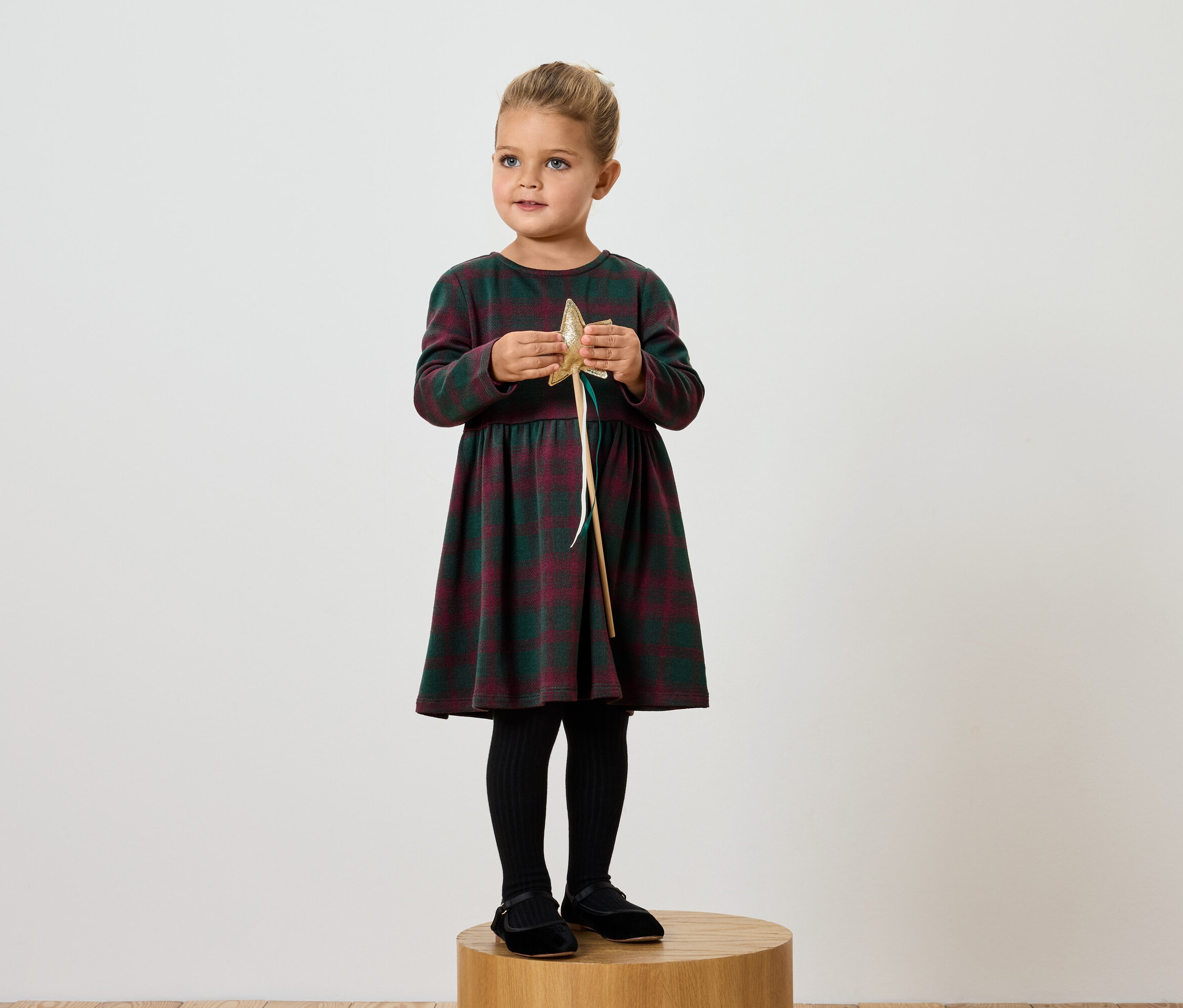 Une fille en robe à carreaux tient une étoile dorée.