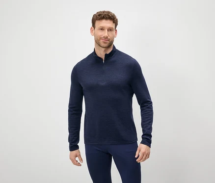 Un homme aux cheveux bruns et à la barbe porte un pull bleu à fermeture éclair et un pantalon bleu.