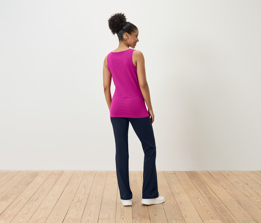 Une femme se tient dos à la caméra, portant un haut rose et un pantalon bleu marine.