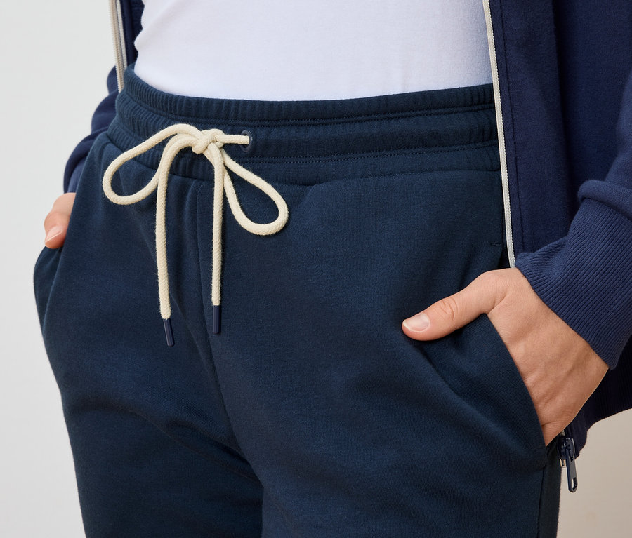 Une personne a les mains dans les poches d'un pantalon de survêtement bleu marine avec un cordon de serrage clair.