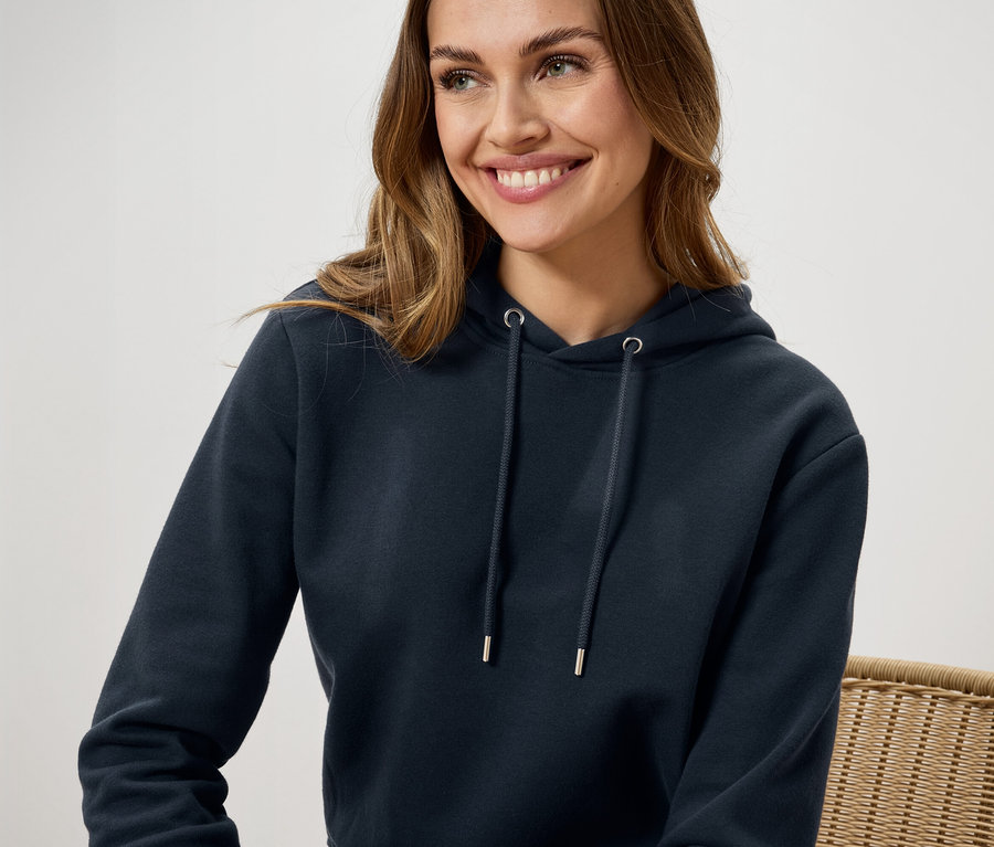 Une femme souriante porte un sweat à capuche bleu foncé.