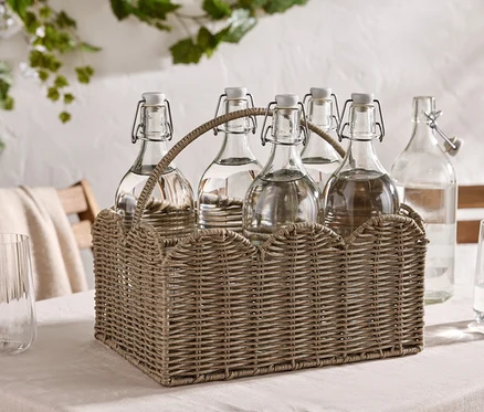 Six bouteilles d'eau à bouchon mécanique dans un panier en osier sur une table, plus deux verres.