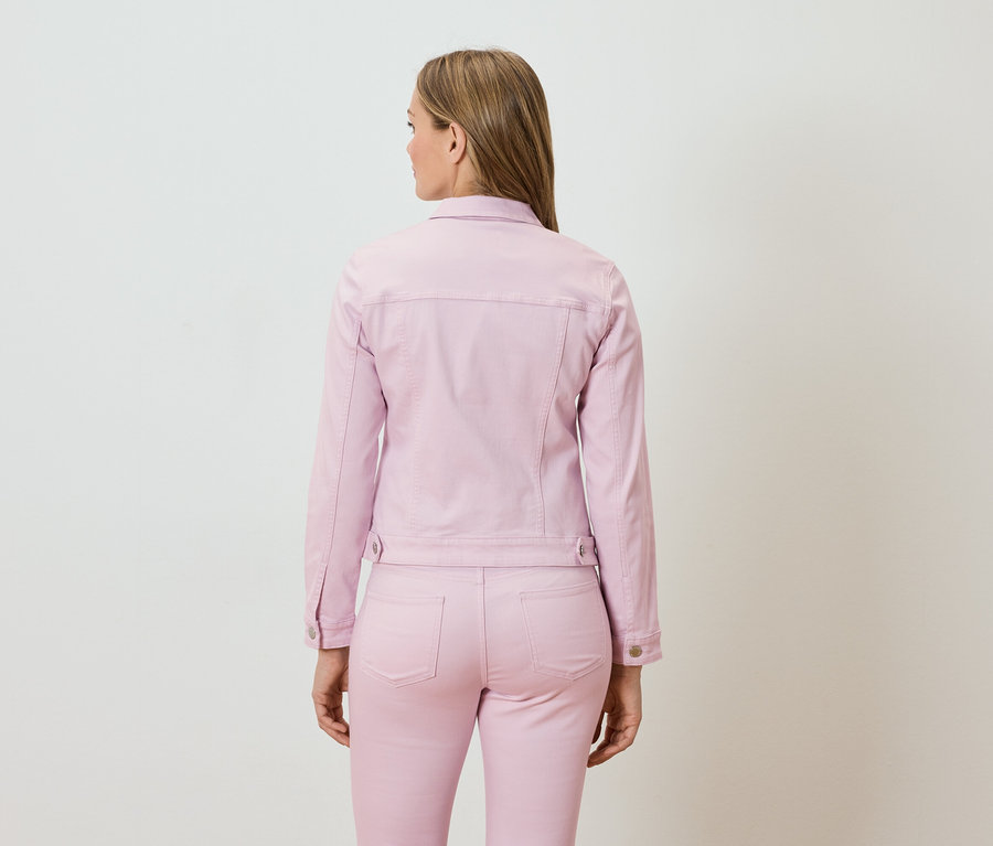 Femme vue de dos, vêtue d'une veste en jean rose et d'un pantalon assorti.