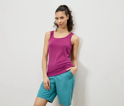 Une femme pose en débardeur rose et short turquoise devant un mur blanc.