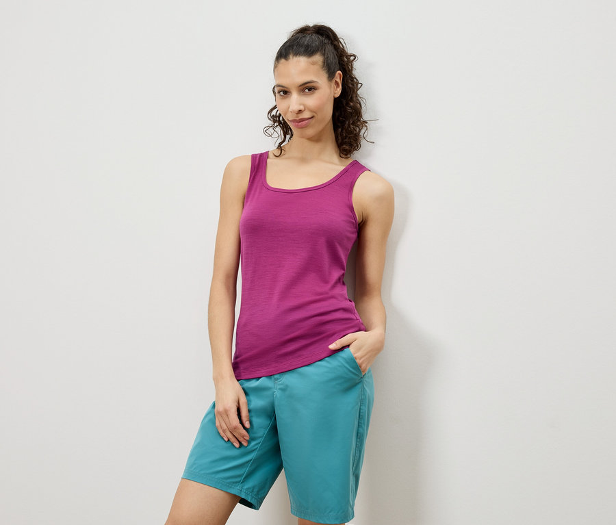 Une femme pose en débardeur rose et short turquoise devant un mur blanc.