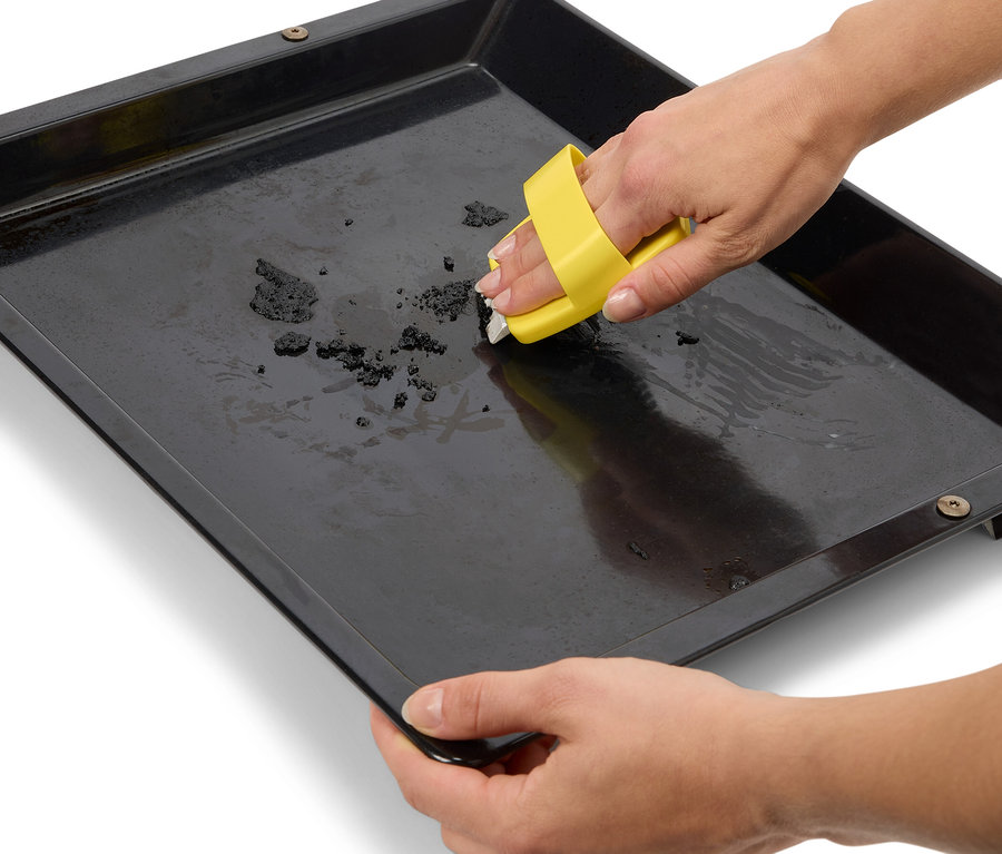 Une personne nettoie une plaque de cuisson noire avec un outil de nettoyage jaune.