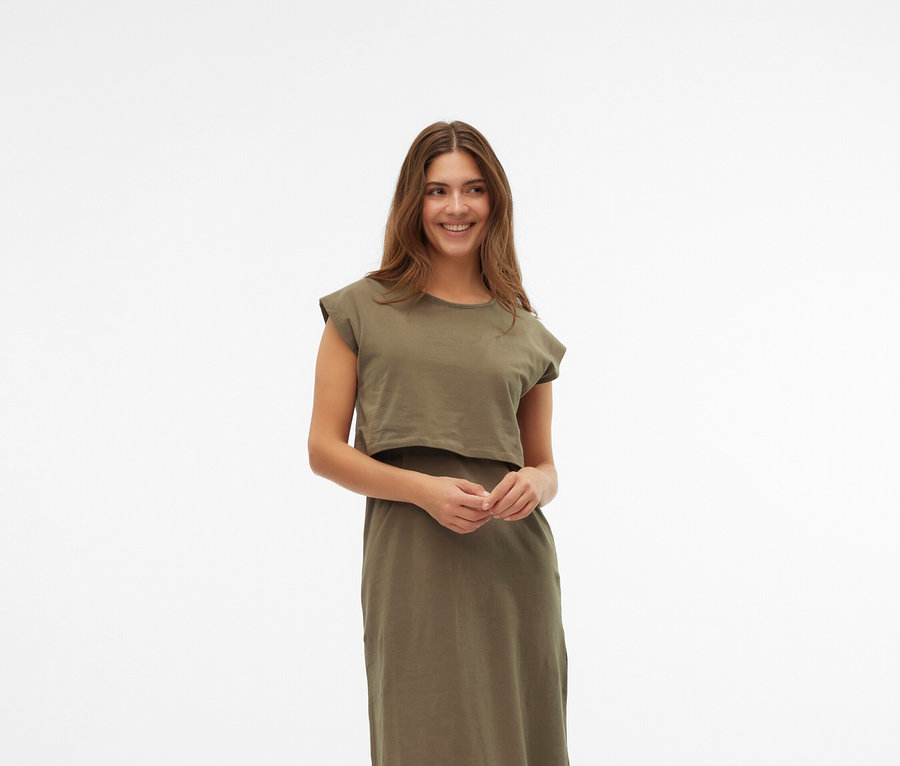 Une femme porte une robe kaki et des chaussures Mary Jane couleur crème sur un fond blanc.