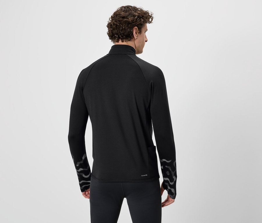 Vue de dos, un homme aux cheveux bouclés porte un haut de sport et un legging noirs. Le haut a un motif sur les manches.