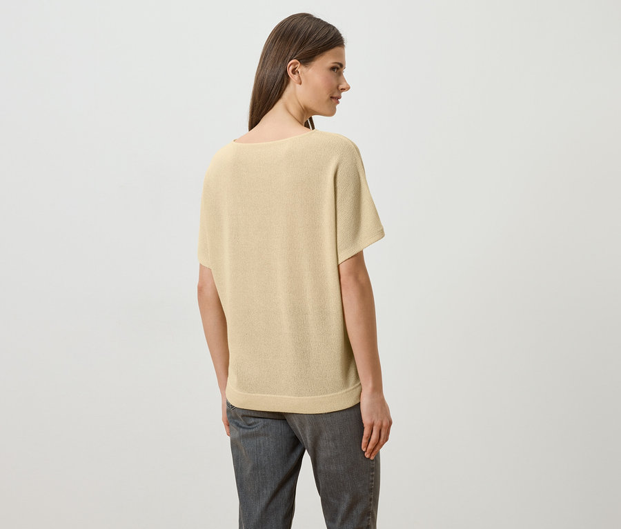 Une femme aux longs cheveux bruns porte un t-shirt jaune clair et un jean gris, vue de dos.