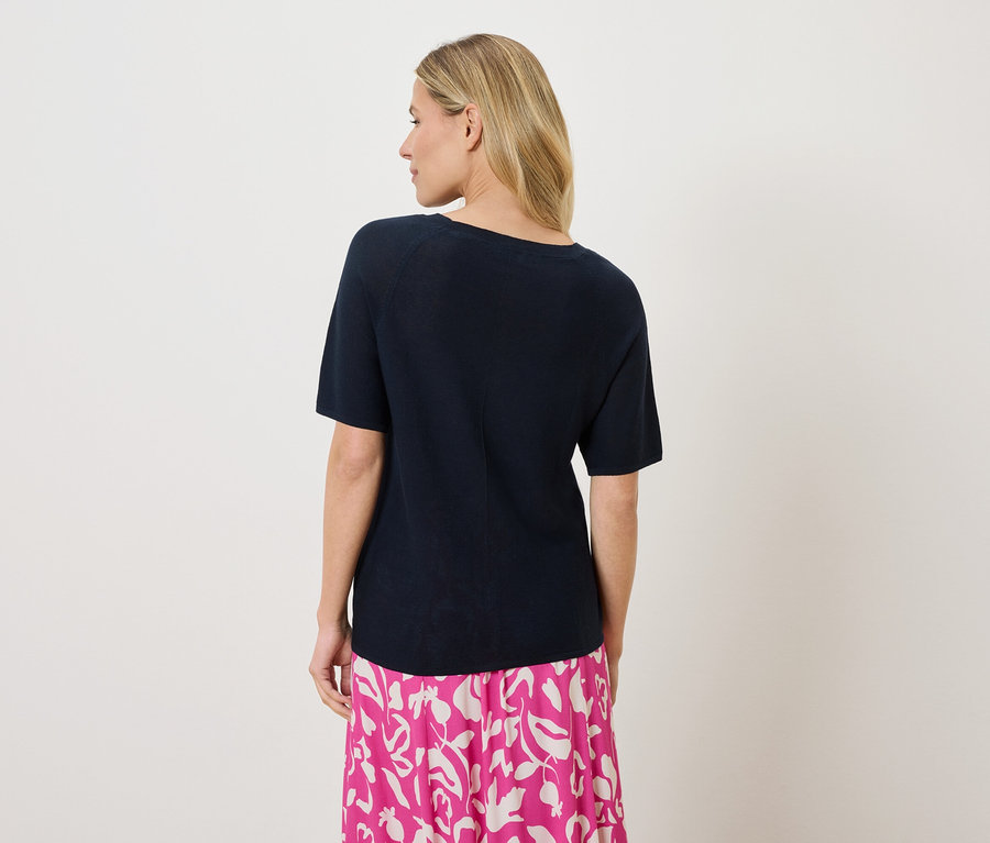 Une femme aux cheveux blonds porte un t-shirt bleu marine et une jupe à motifs rose et blanc, vue de dos.