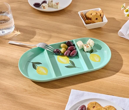 Sur une table en bois se trouve un plateau de service allongé vert menthe avec un motif de citron, des olives, des dés de fromage et une fourchette.
