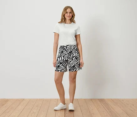 Femme debout en t-shirt blanc et short à motifs.
