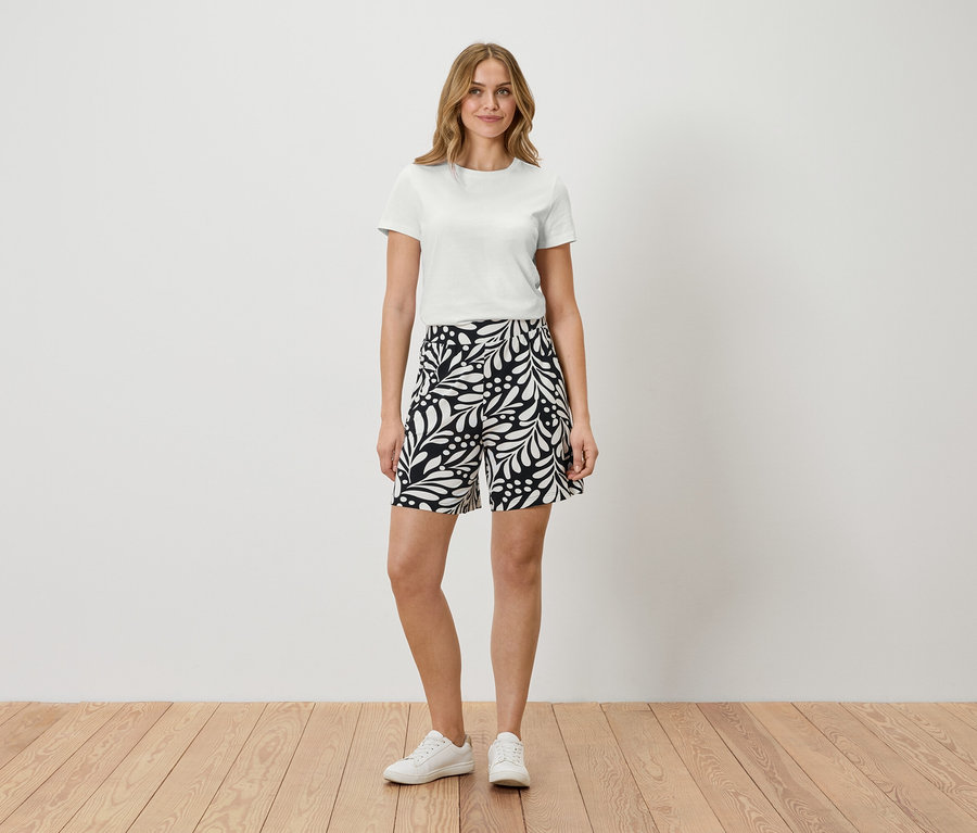 Femme debout en t-shirt blanc et short à motifs.