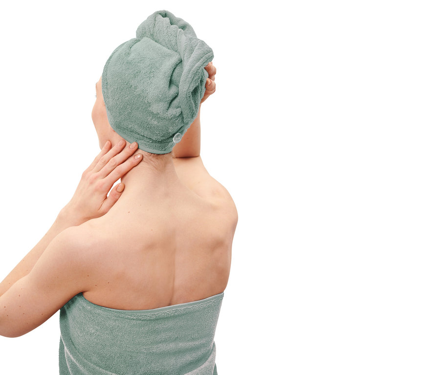 Femme avec un turban de serviette vert et une serviette assortie autour du corps, posant ses mains sur son cou.