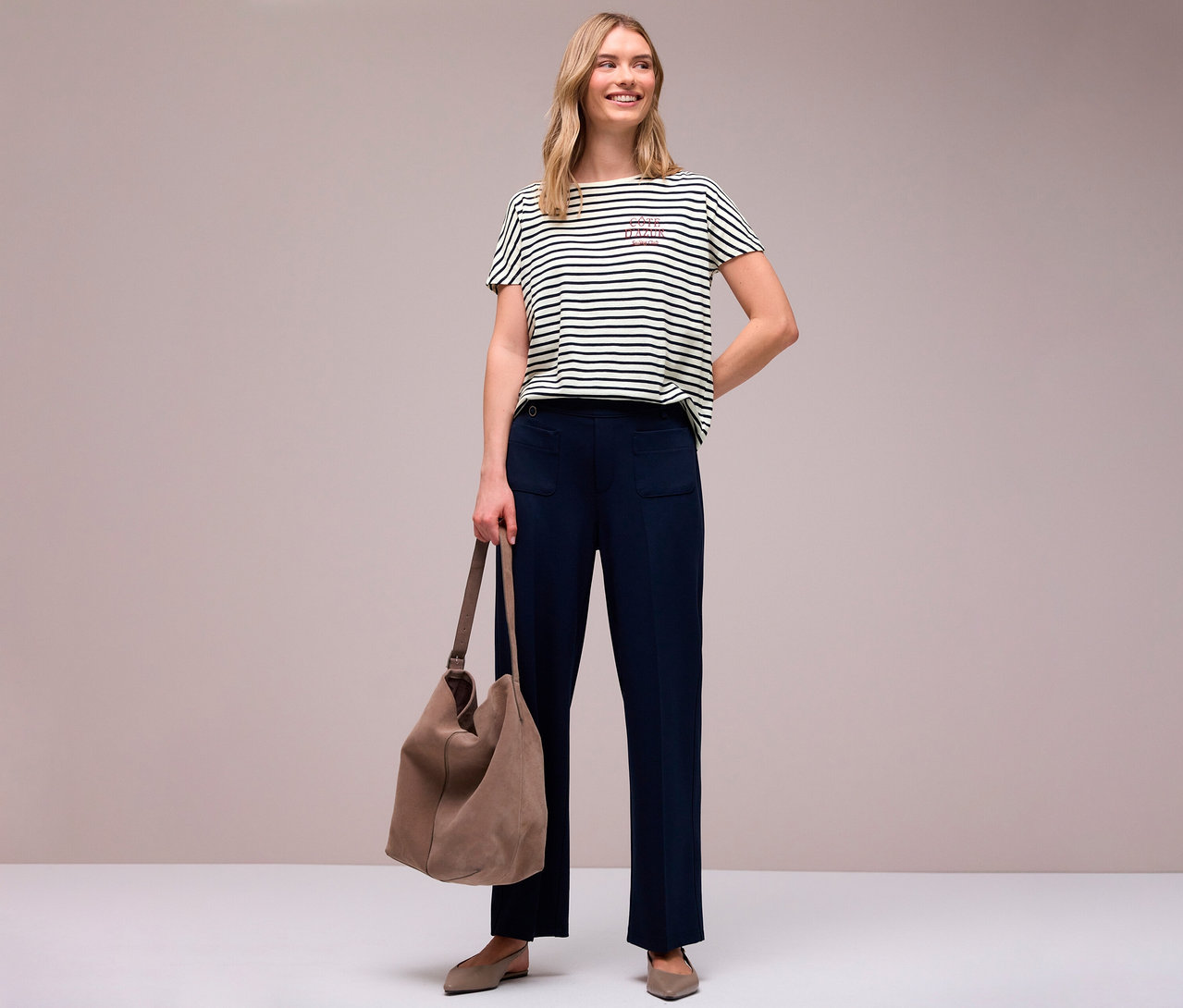 Femme portant un pantalon bleu marine avec poche et un t-shirt Street One bleu marine et blanc rayé avec un lettrage, tenant un sac.