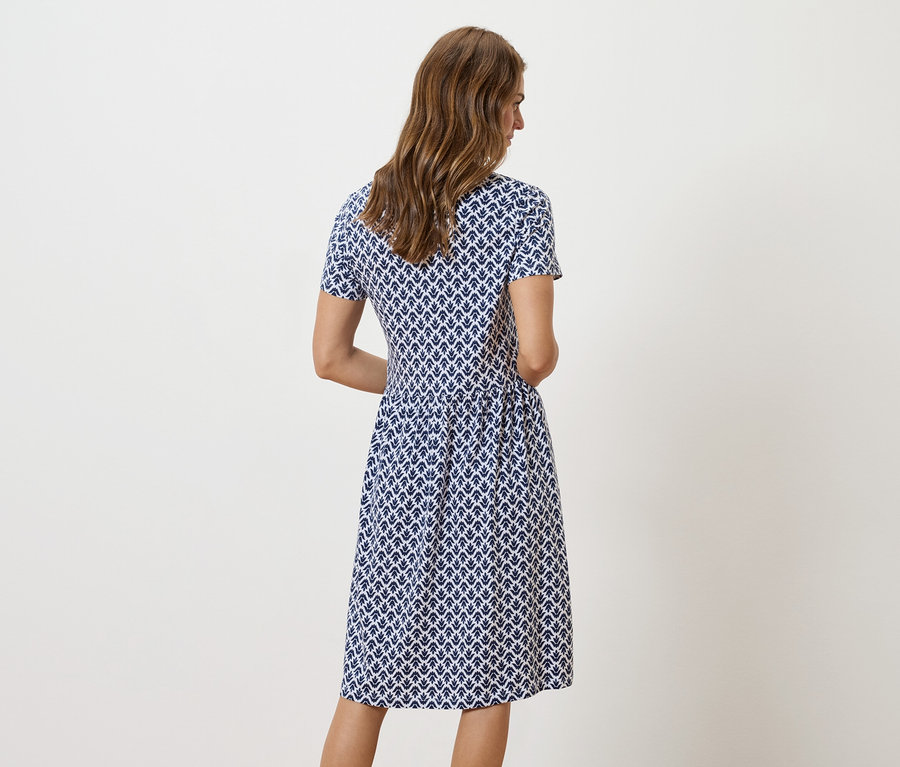 Une femme se tient dos à la caméra, portant une robe à motifs bleu et blanc.