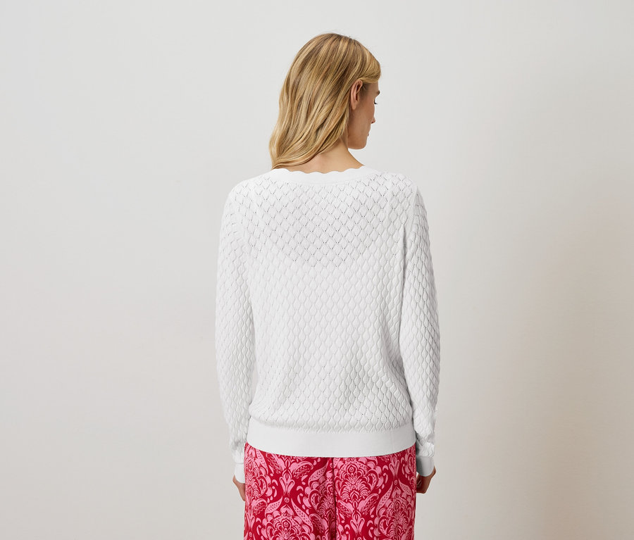 Vue arrière d'une femme blonde portant un pull en tricot blanc et un pantalon rose à motifs.