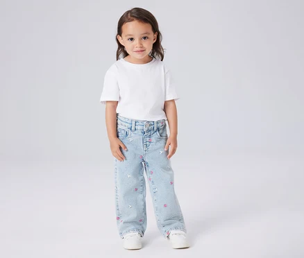 Fillette portant un t-shirt blanc et un jean bleu clair avec des motifs de cœurs et de souris.