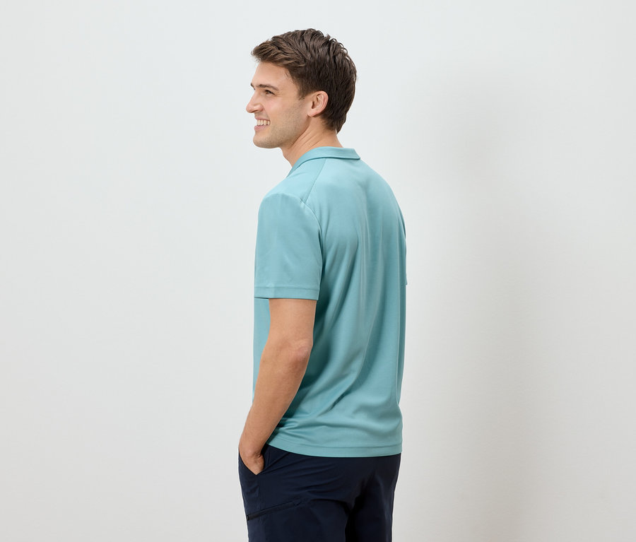Homme de profil portant un polo bleu clair et un pantalon foncé.