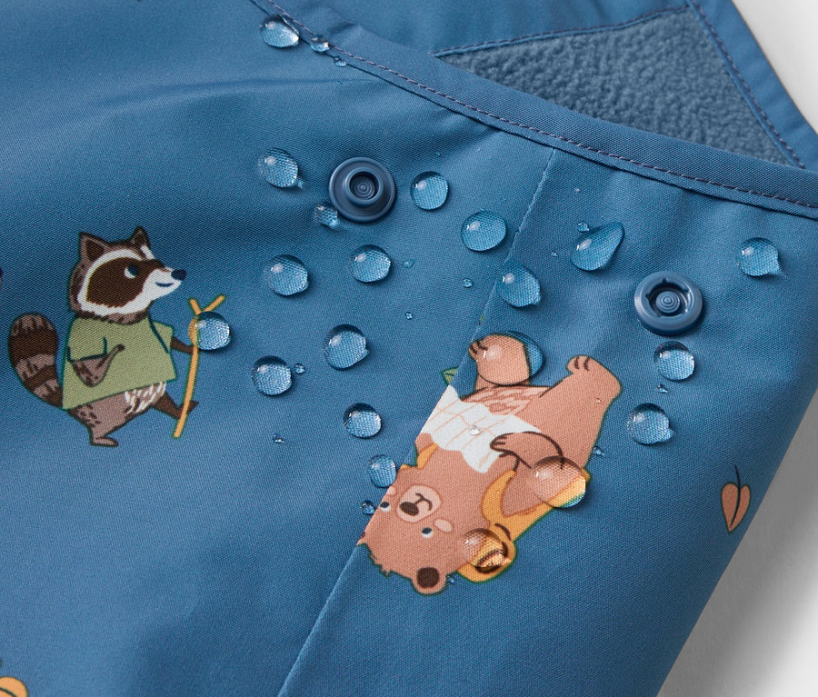 Gros plan d'un tissu bleu avec des fermetures à boutons, des gouttes d'eau et des motifs d'ours et de ratons laveurs.