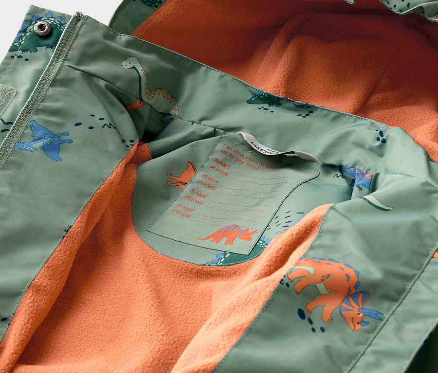 Vue intérieure d'une veste ouverte vert clair à motifs de dinosaures avec une doublure en polaire orange.