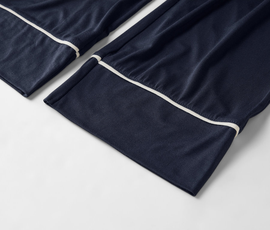 Gros plan d'un pantalon de pyjama bleu marine avec des passepoils blancs sur fond blanc.