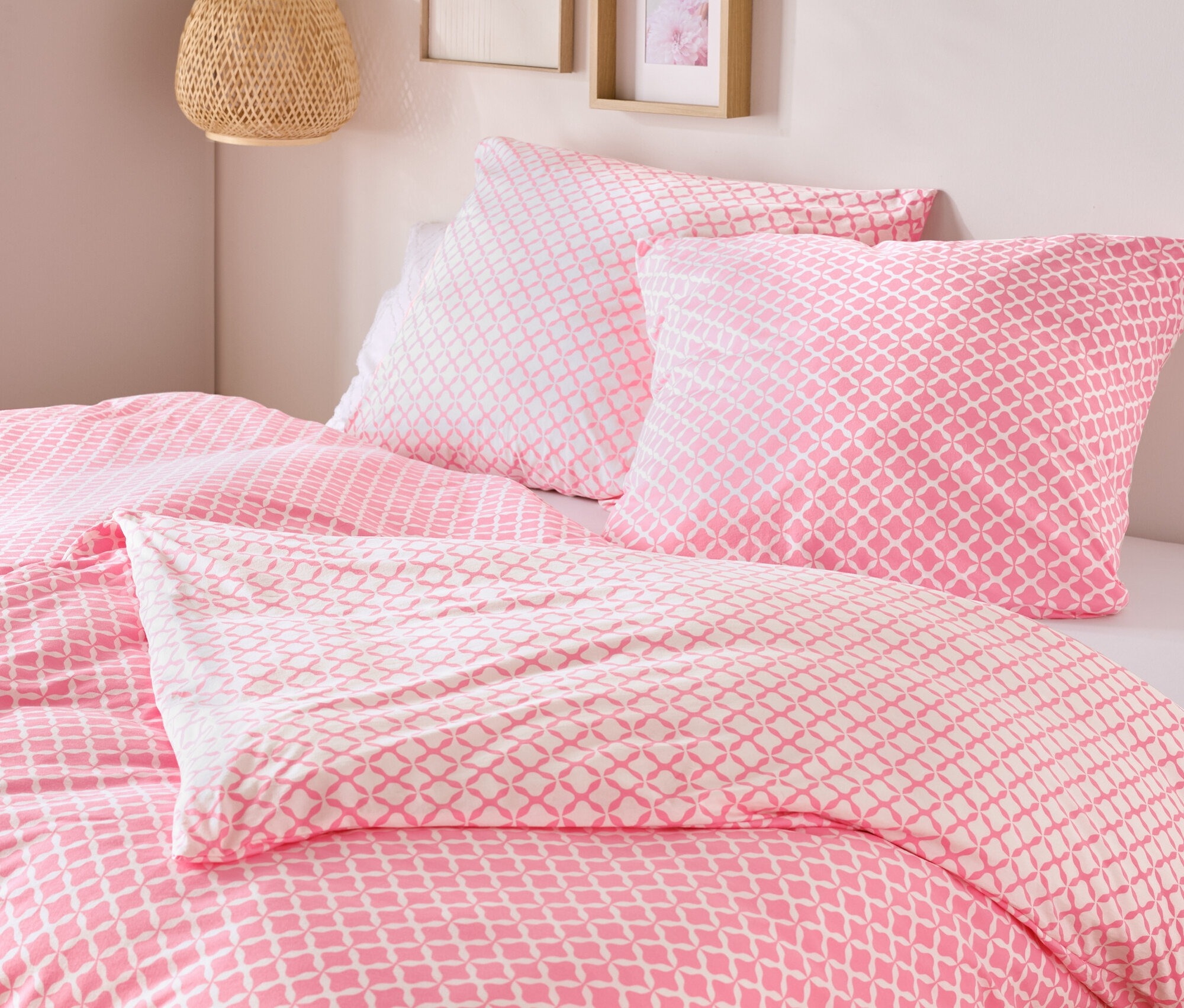 Gros plan d'un lit avec du linge de lit en jersey rose et blanc, taille standard et king size, avec deux oreillers et une couette.
