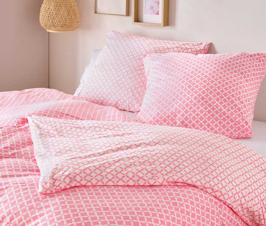 Gros plan d'un lit avec du linge de lit en jersey rose et blanc, taille standard et king size, avec deux oreillers et une couette.