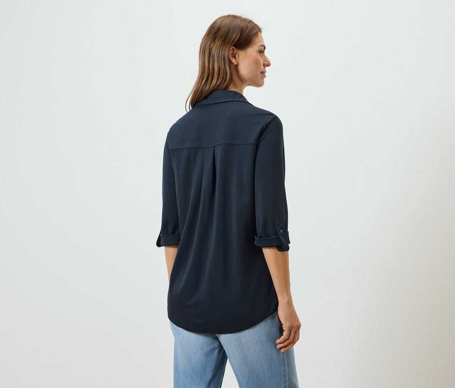 Vue arrière d'une femme aux longs cheveux bruns portant une chemise bleu marine et un jean bleu clair.