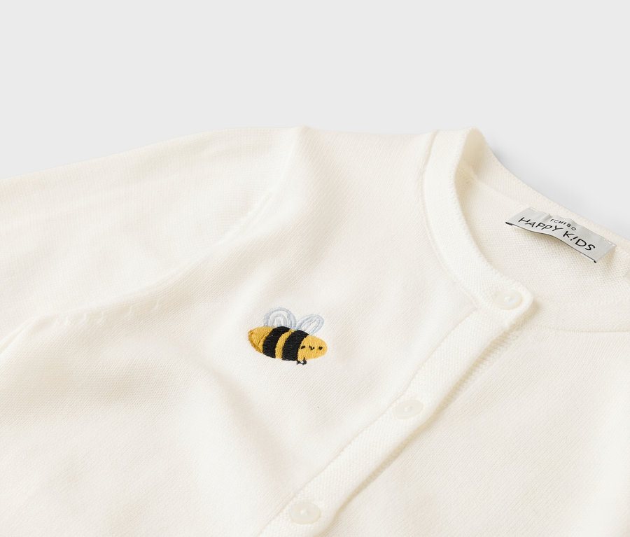 Gros plan d'un cardigan tricoté blanc avec patte de boutonnage et abeille brodée.