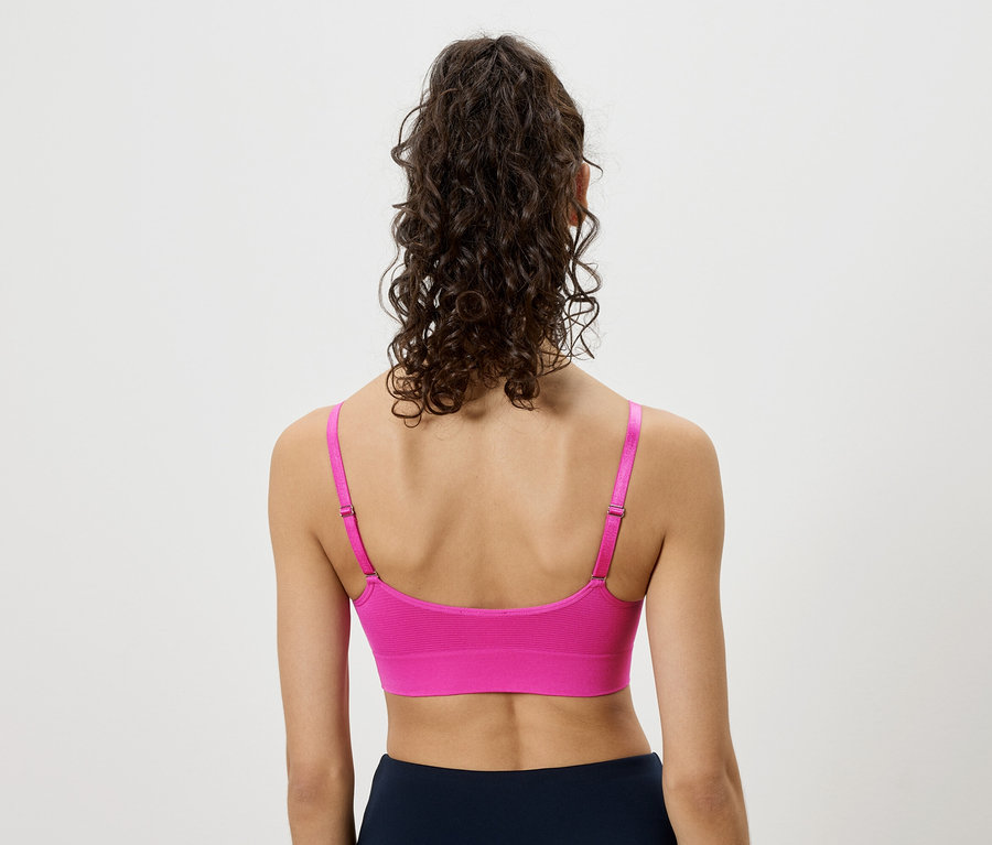 Vue de dos d'une femme aux cheveux bouclés relevés, portant un soutien-gorge de sport rose et un legging bleu marine.