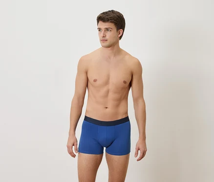 Homme torse nu portant un boxer bleu sur un fond blanc.