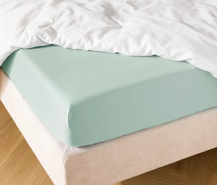 Gros plan d'un lit avec un drap-housse bleu clair et une couette blanche.