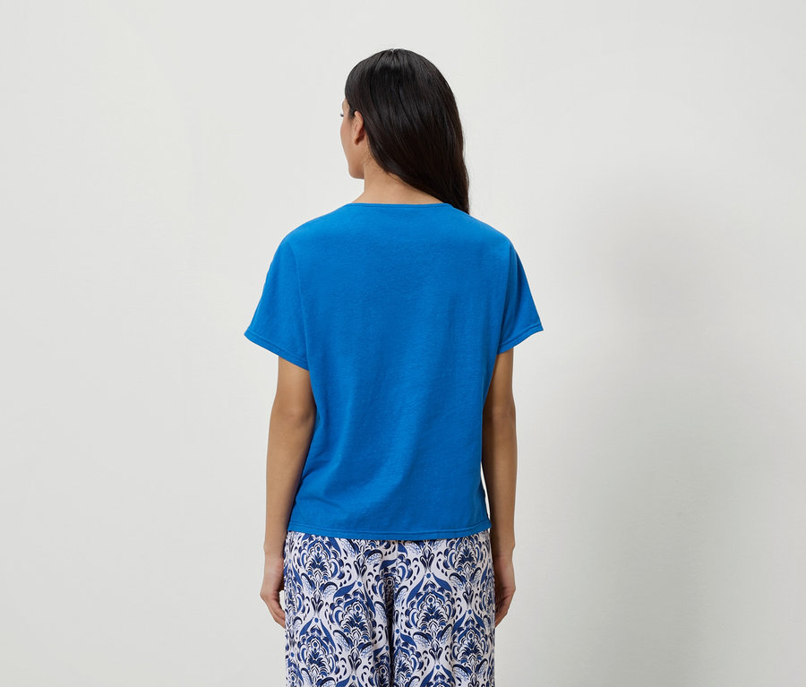 Vue de dos d'une femme aux cheveux foncés portant un t-shirt bleu et un pantalon à motifs bleu et blanc.