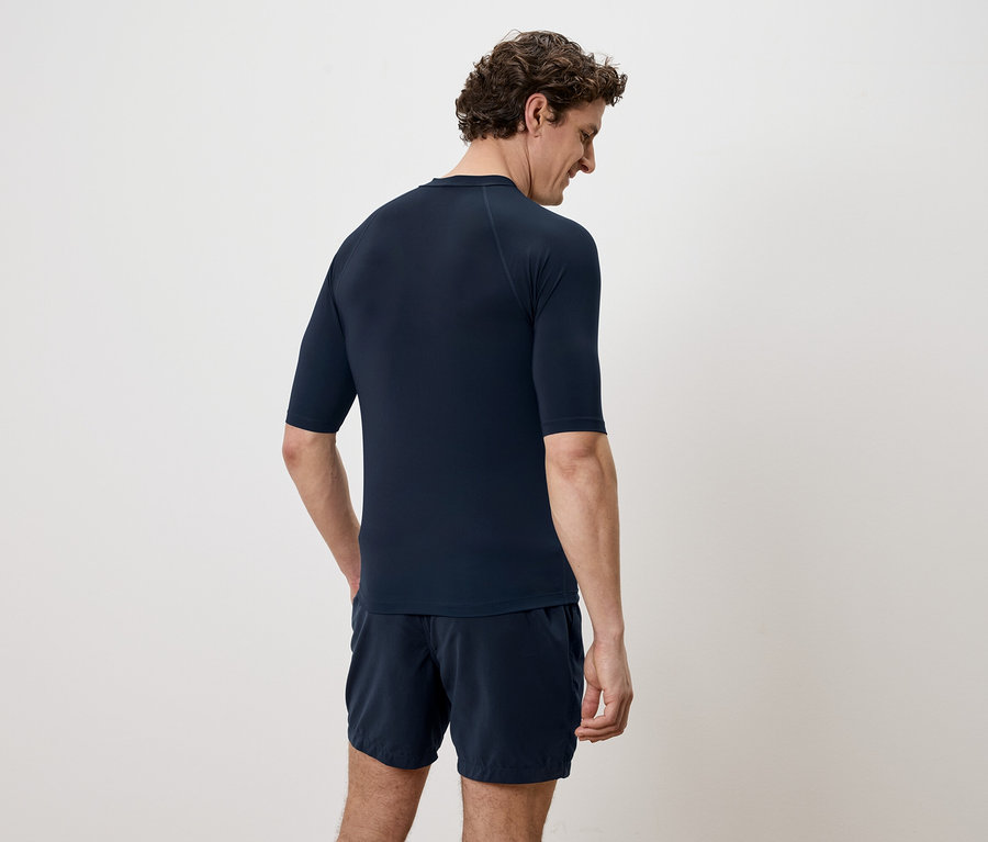 Homme vu de dos portant un t-shirt à manches courtes bleu marine et un short sur fond blanc.