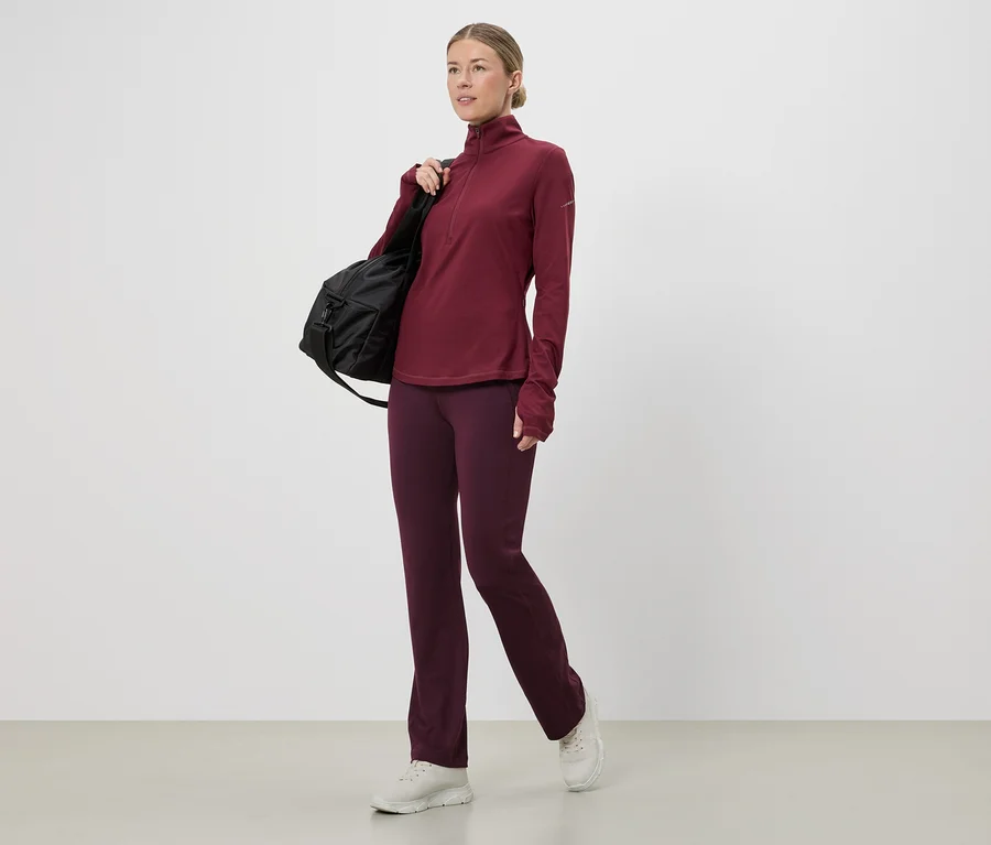 Femme portant un haut et un pantalon de sport bordeaux avec un sac noir sur l'épaule, baskets blanches.