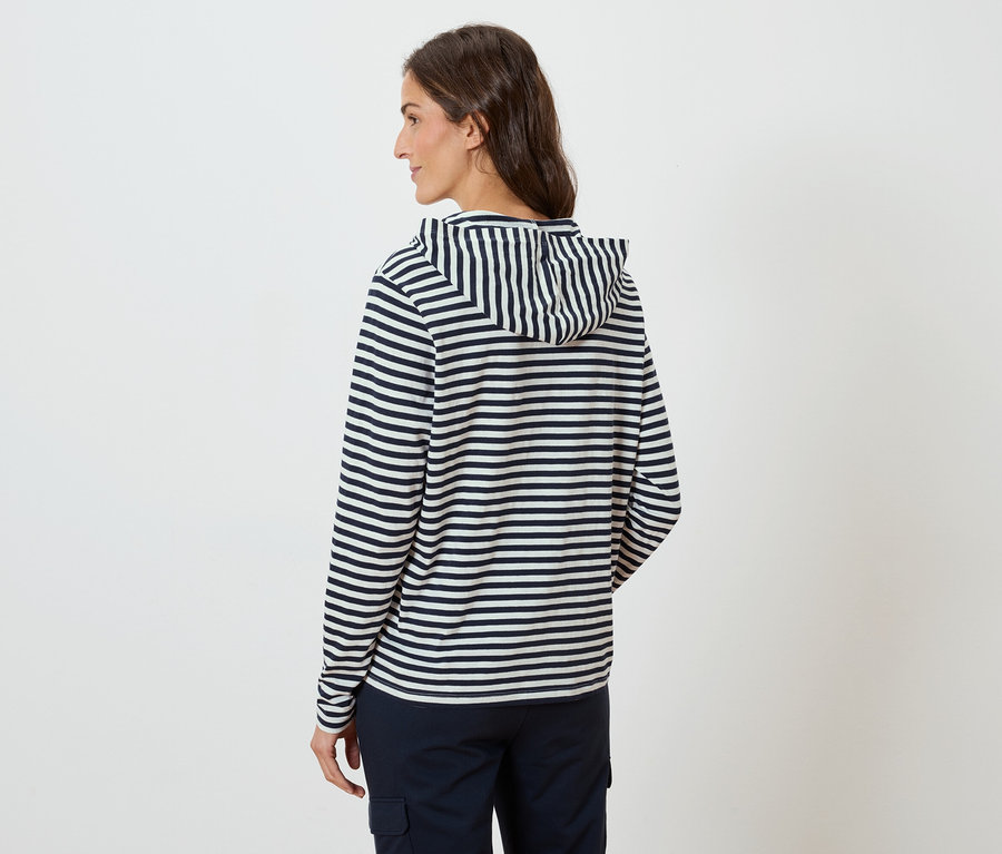Femme de dos, portant un sweat à capuche rayé et un pantalon bleu marine.