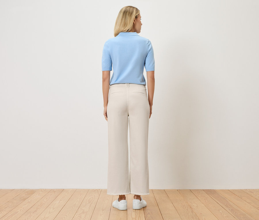 Vue de dos d'une femme blonde portant un polo bleu clair, un pantalon beige et des chaussures blanches.