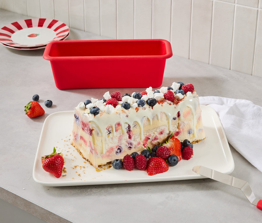 Dessert glacé aux baies sur une assiette, à côté d'un moule à gâteau rouge et d'assiettes à rayures rouges.