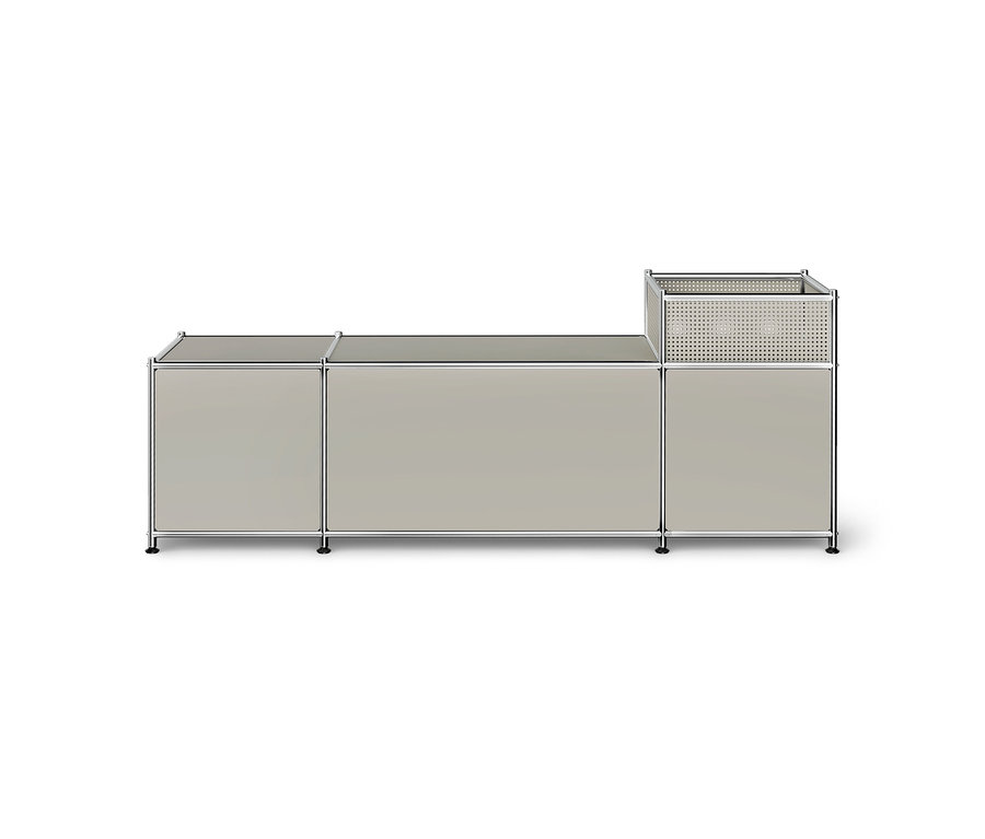 Meuble de rangement modulaire gris clair avec cadre chromé, comprenant deux armoires basses et une section droite plus haute avec un panier perforé sur le dessus, sur fond blanc.