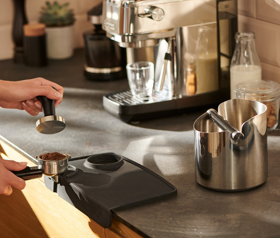 Une femme tasse le café sur un tapis de tassage noir.