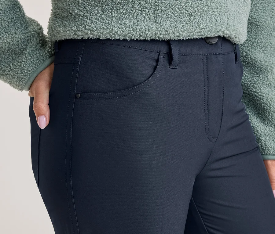 Personne portant un pantalon bleu foncé et un haut en polaire vert clair. La main droite avec du vernis à ongles rose est dans la poche du pantalon.