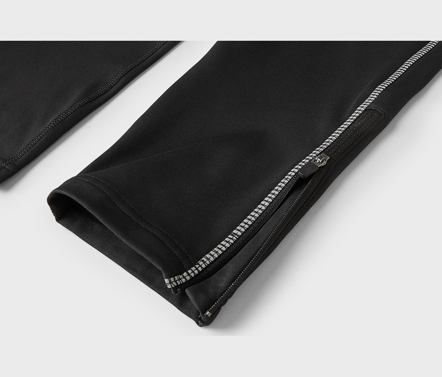 Gros plan d'un pantalon de sport noir avec une fermeture éclair à la cheville partiellement ouverte, présentant des détails réfléchissants.
